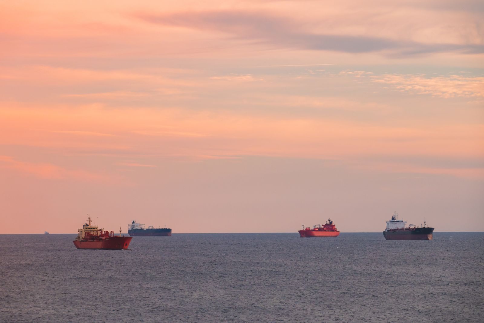 Ships spread along the horizon on a calm sea under a pink sunset sky