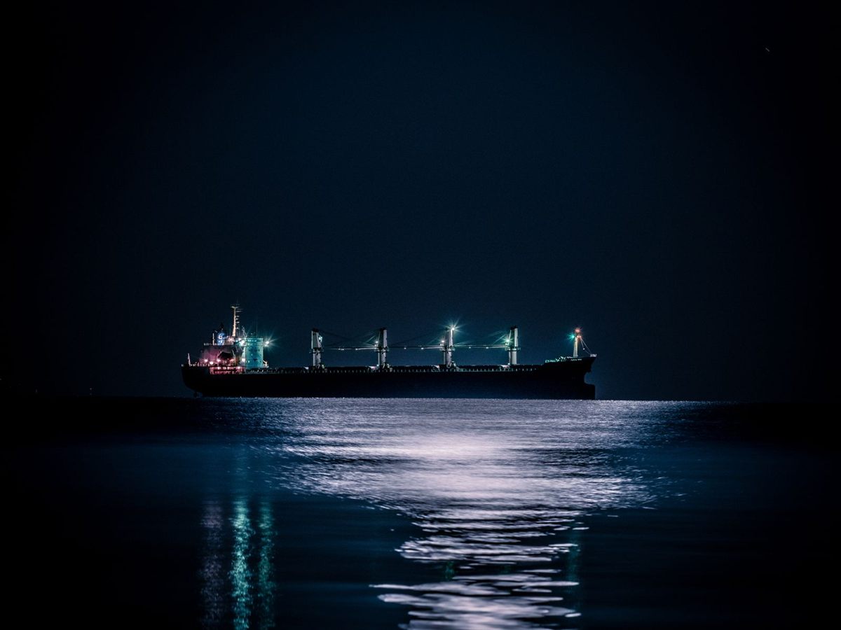 A ship lit up at night on a dark sea with moonlight on the water