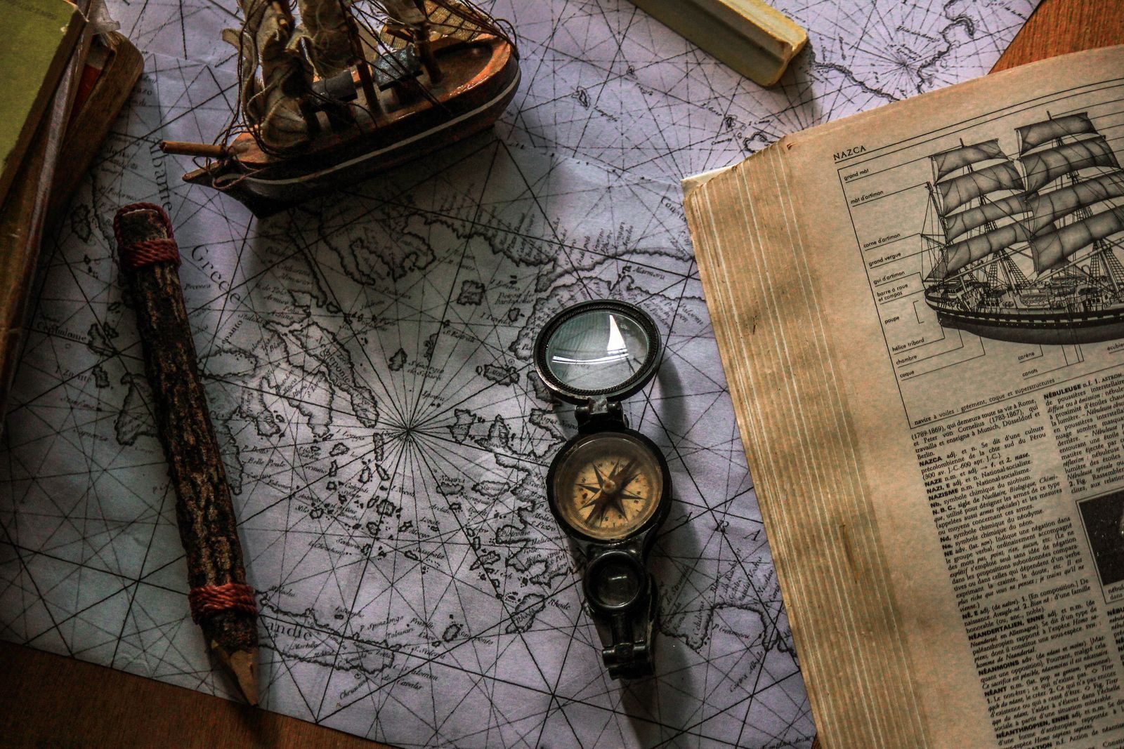 An old nautical chart with a compass, telescope and ship model, the tools behind nautical miles on a cruise