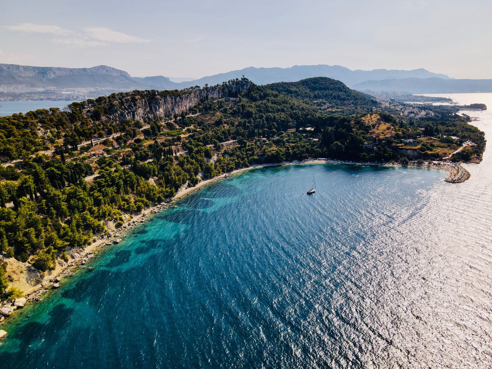 Aerial view of a wooded coastline and a turquoise bay, showing how far ships sail from shore
