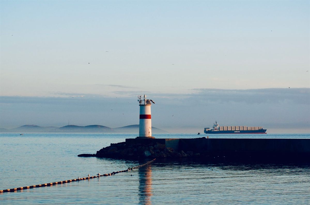 A harbor lighthouse at the end of a breakwater with a cargo ship passing offshore