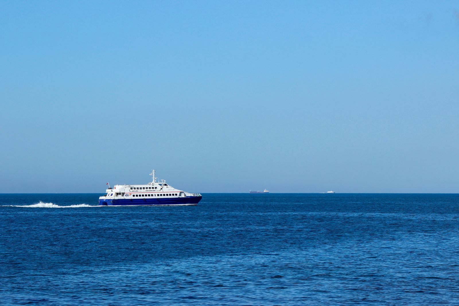 A white passenger ship at speed across open blue water, leaving a long wake at its cruise ship top speed